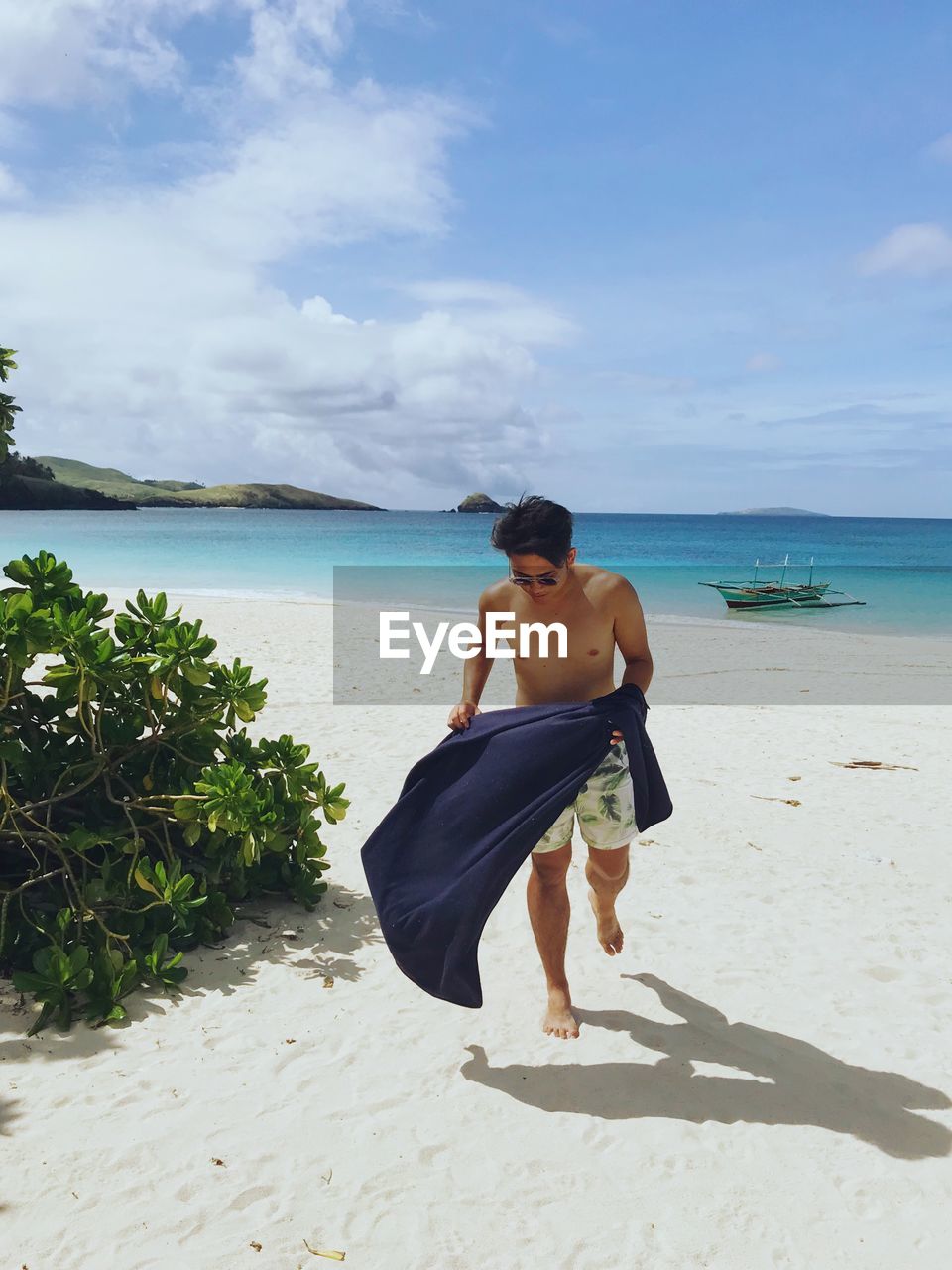 Full length of shirtless man walking at beach against sky