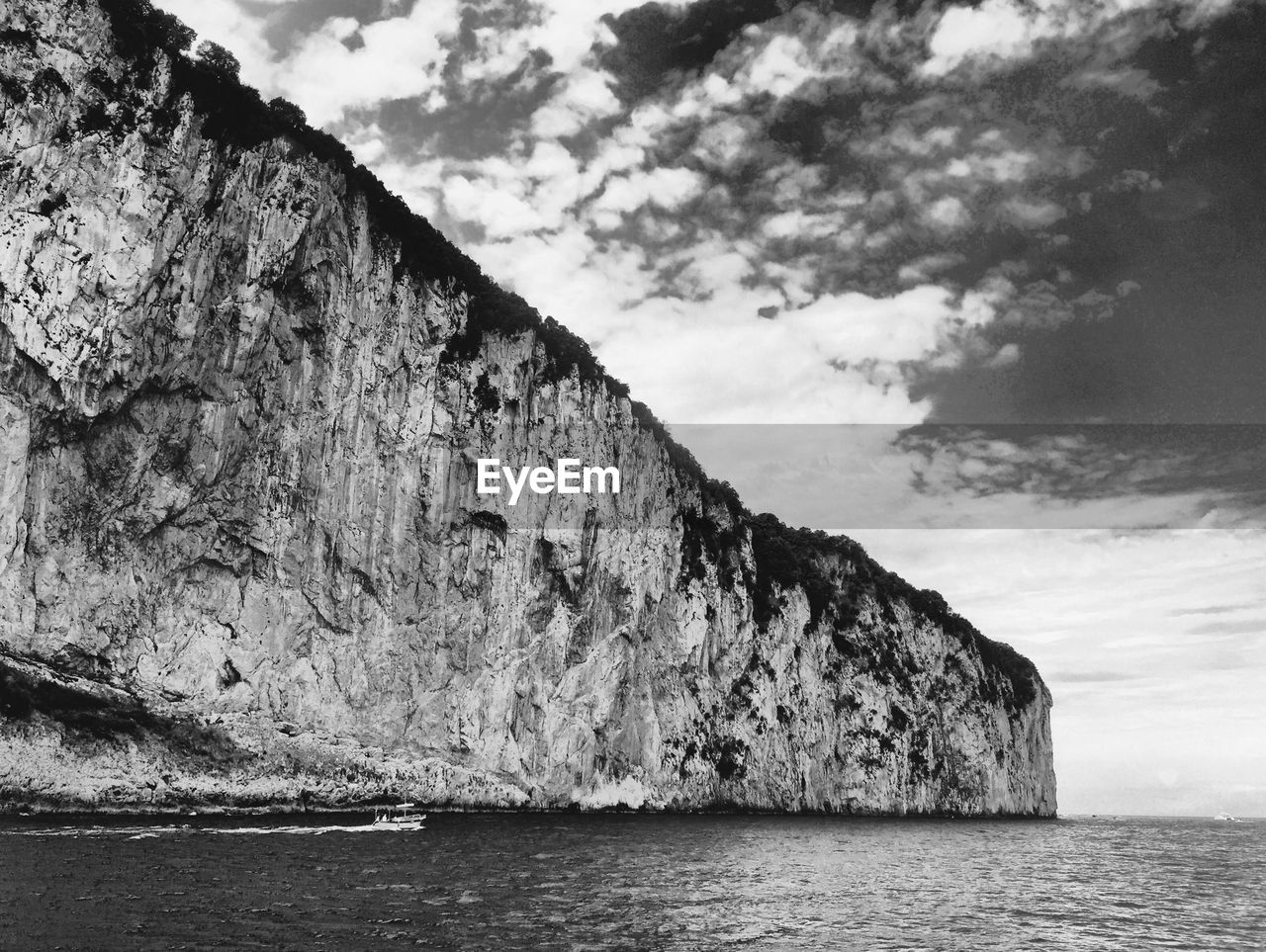 Cliff by sea against cloudy sky