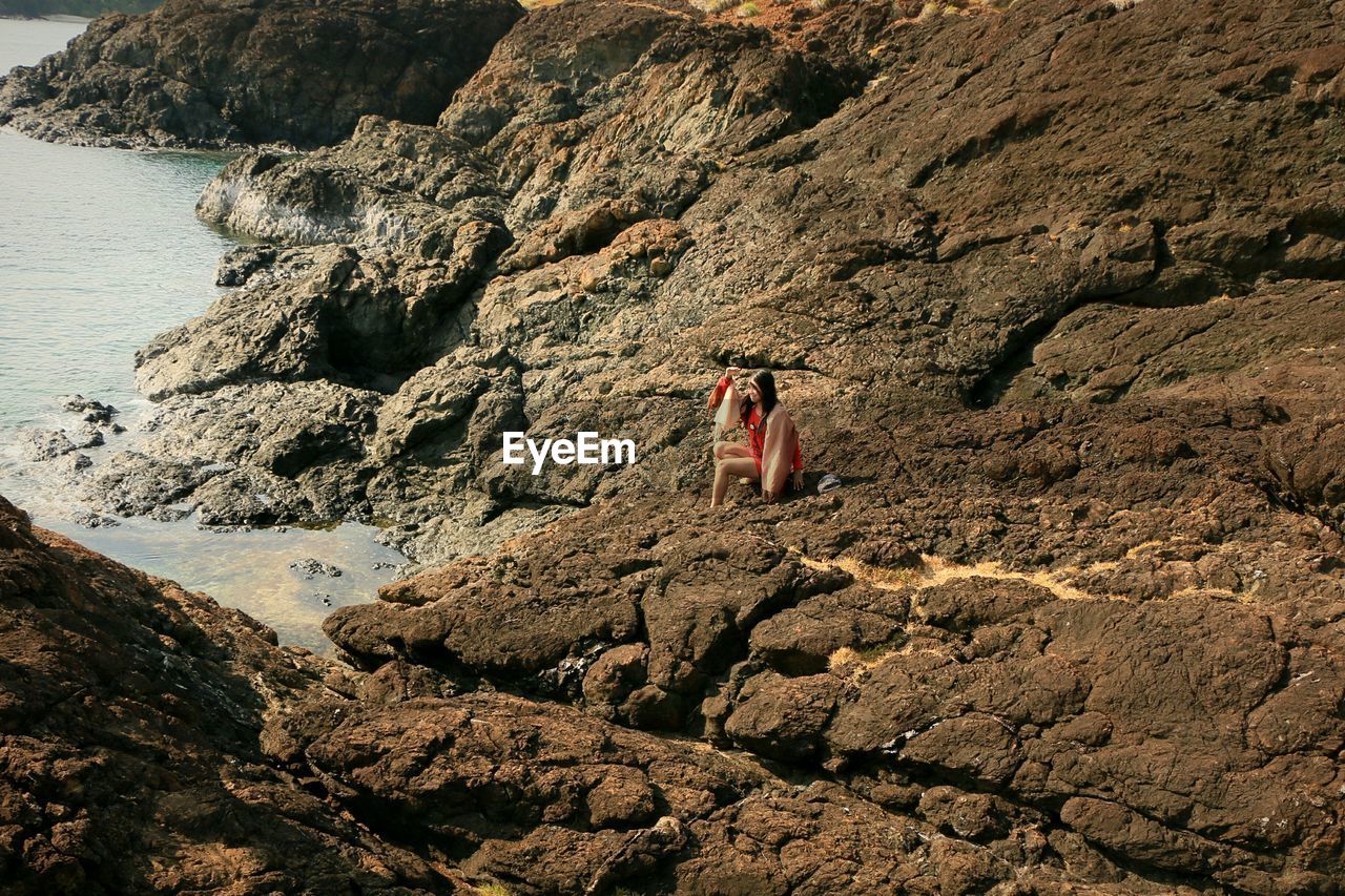 High angle view of woman on rock at beach during sunny day