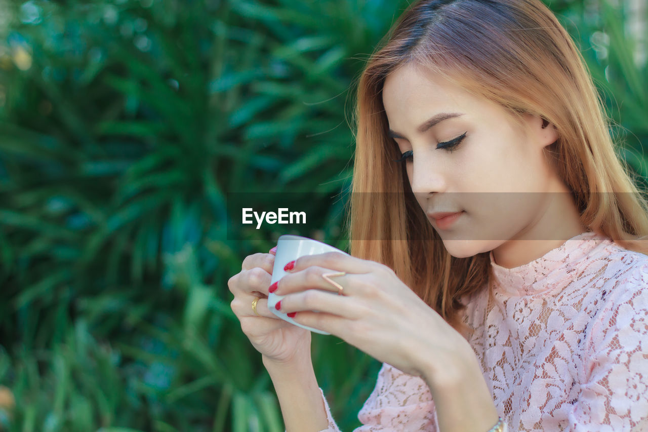 Young woman holding coffee cup against plants