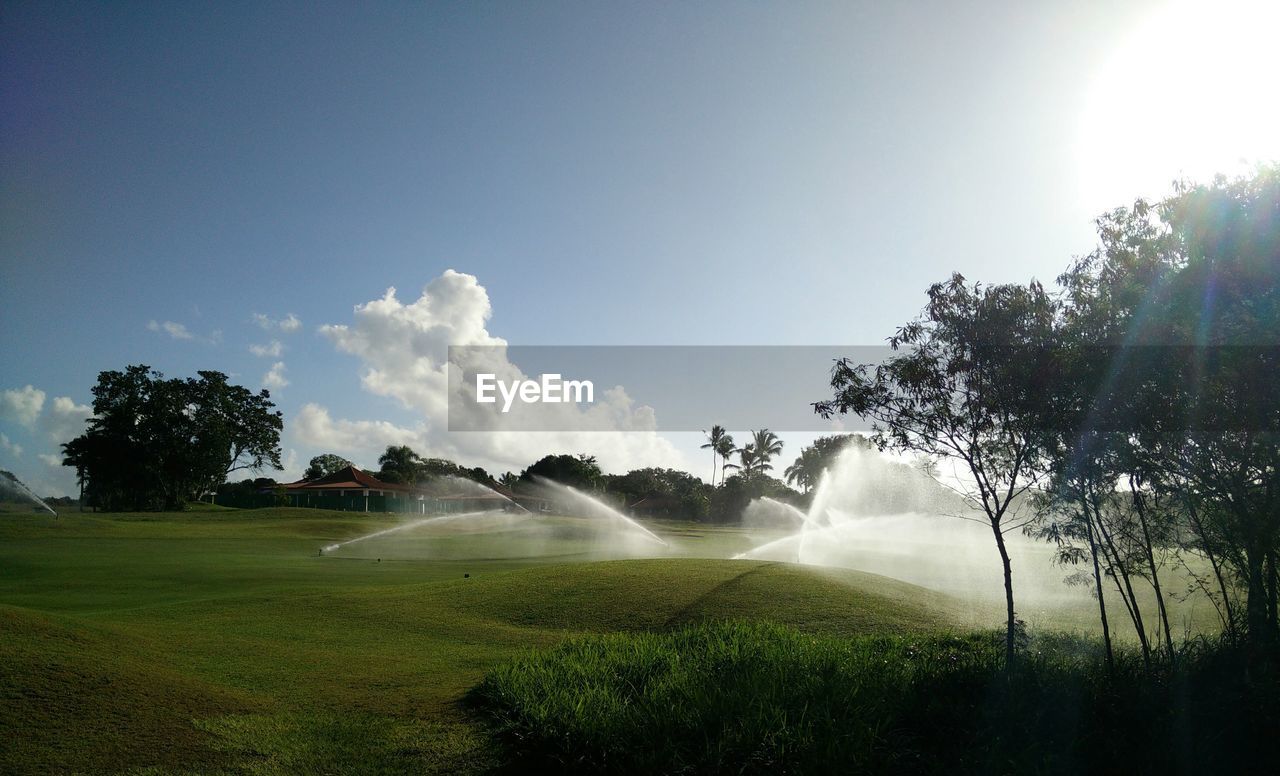 Irrigation sprinkler on golf course against sky on sunny day