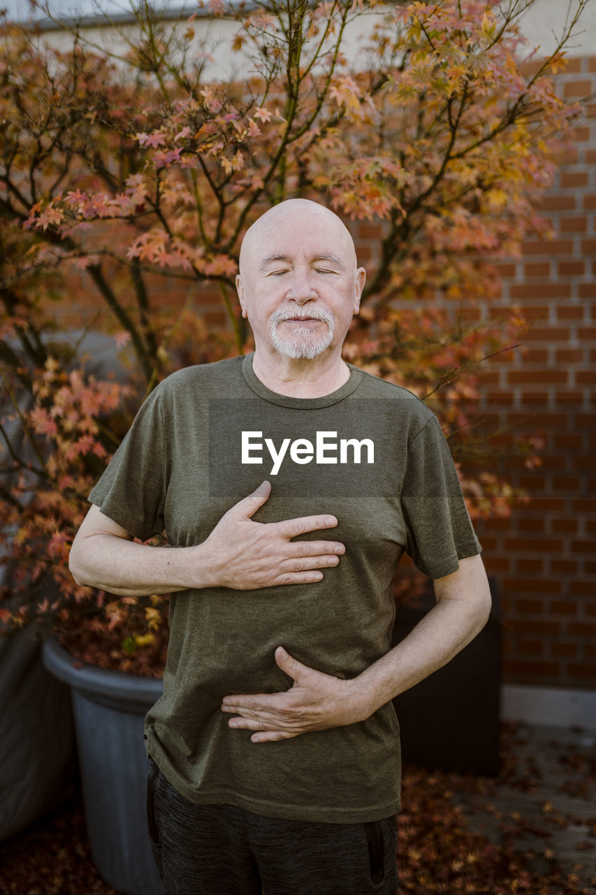 Senior man doing breathing exercise while standing against plant