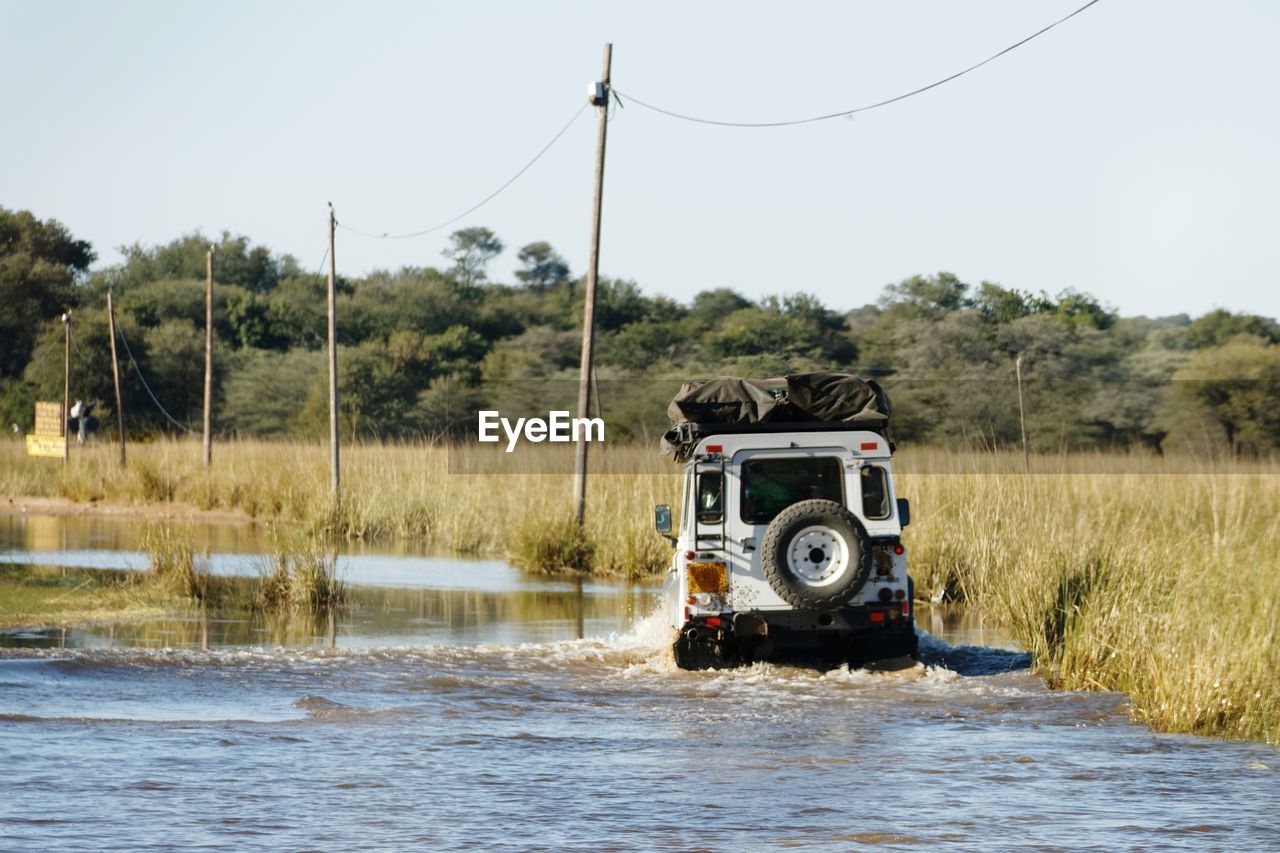 Vintage rough terrain safari car driving through flooded road against clear sky