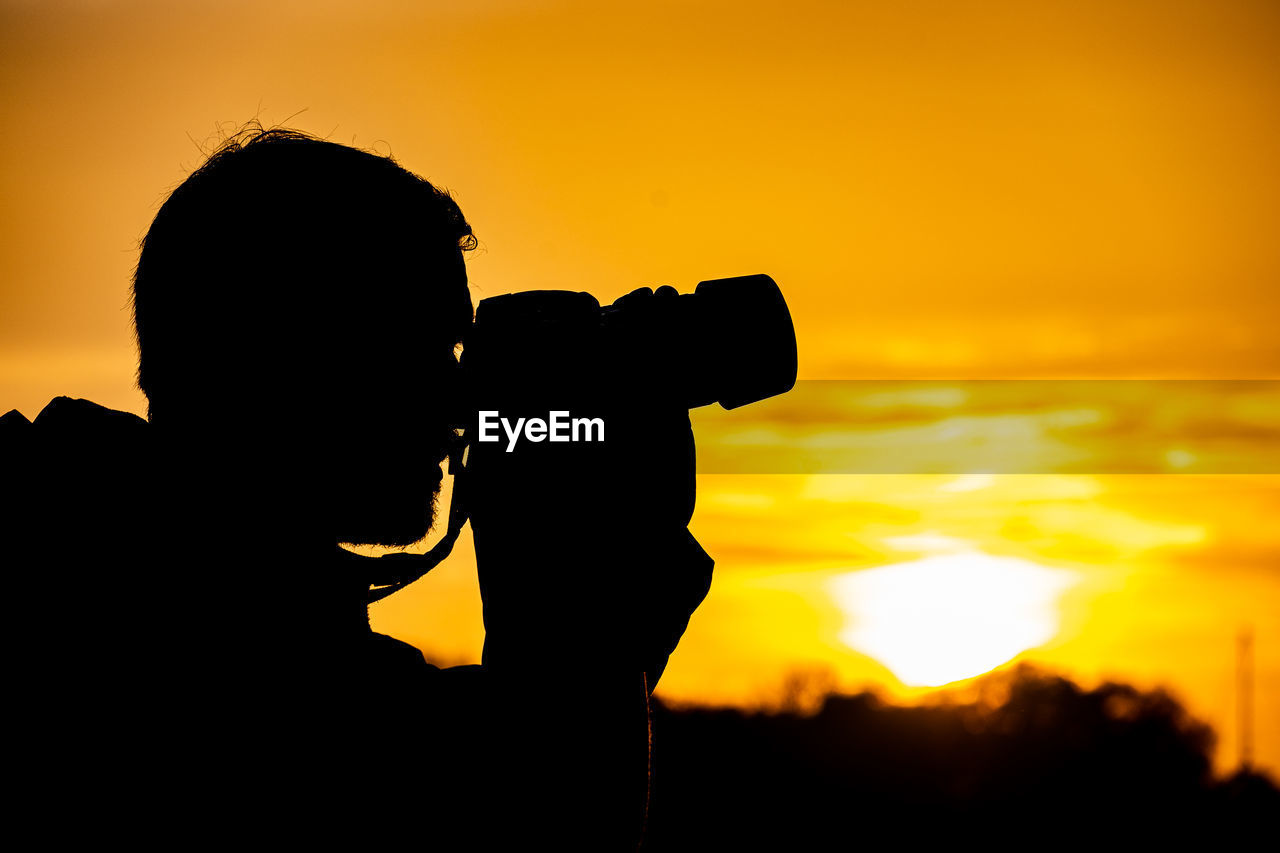 Silhouette man photographing against sky during sunset