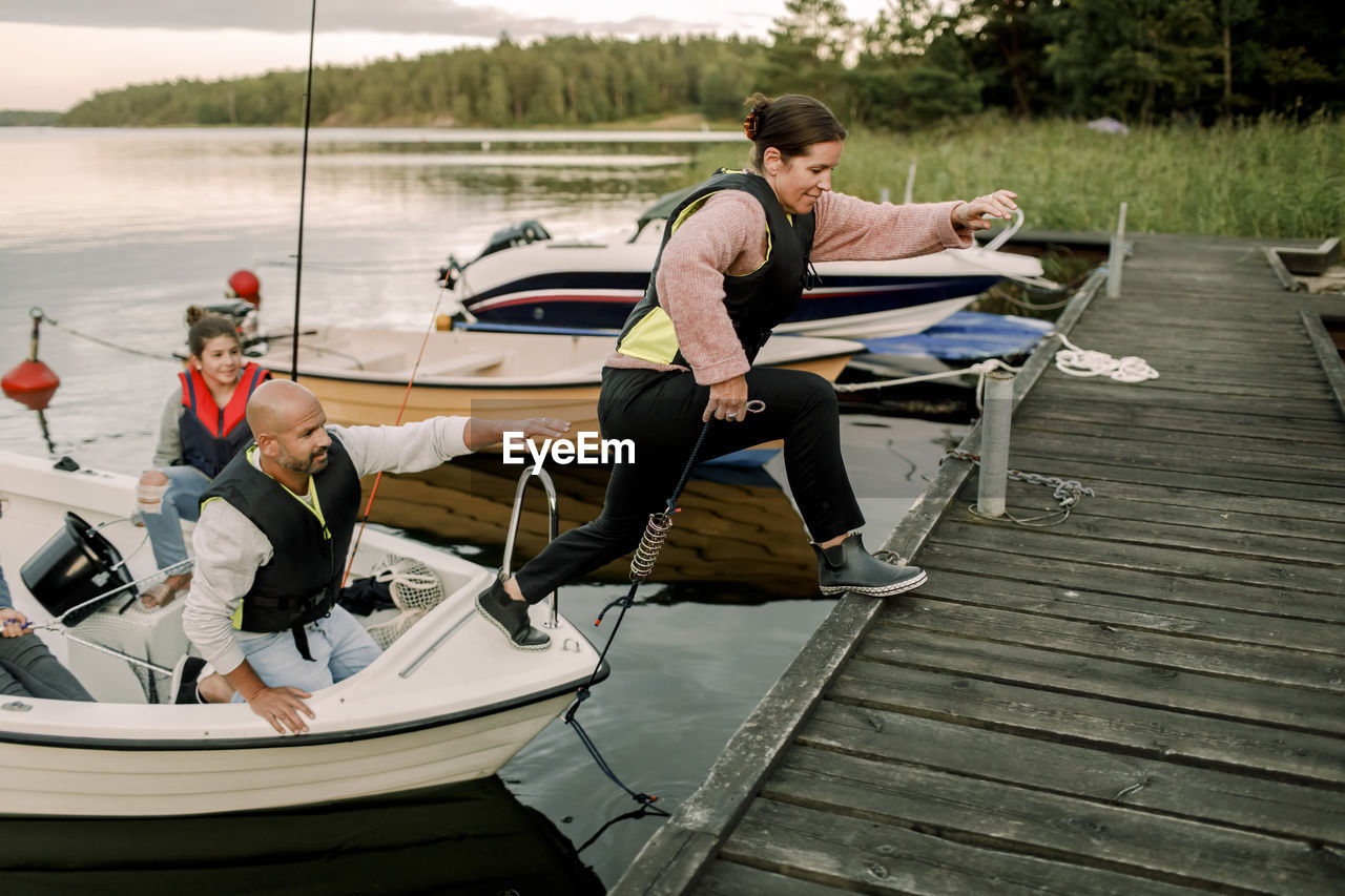 Family looking at woman jumping on pier from boat during summer