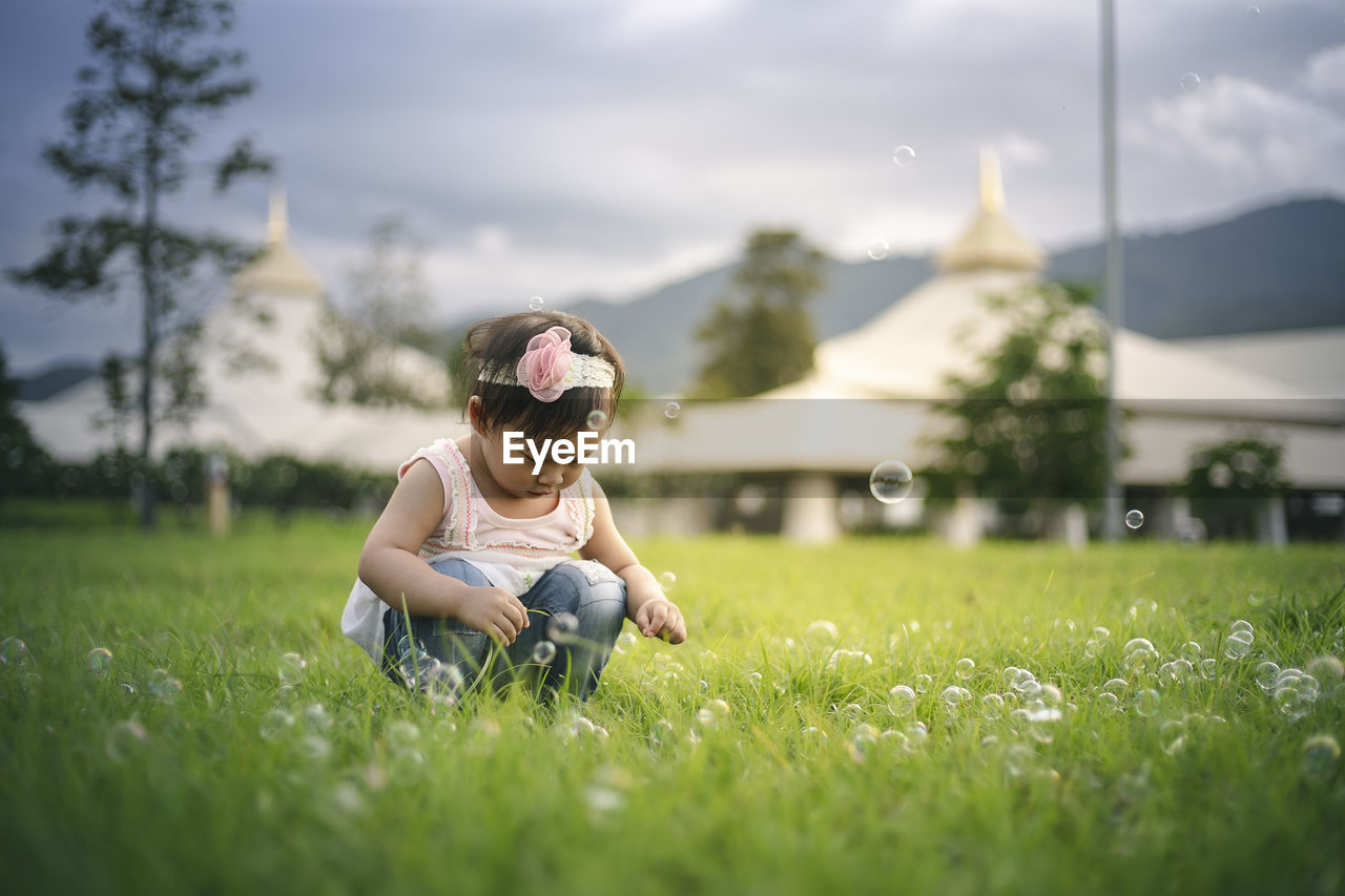 Baby girl crouching on grassy land