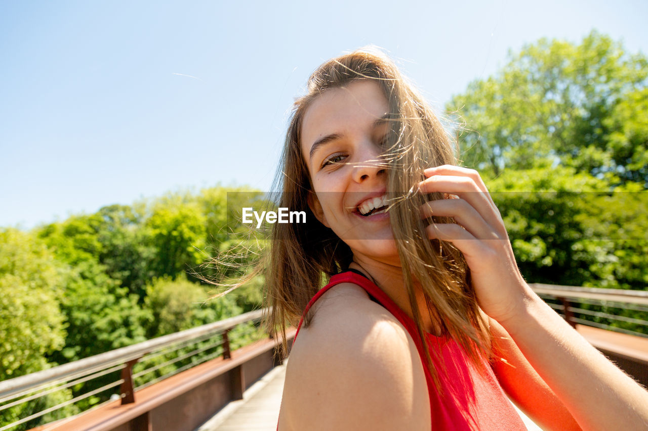 Portrait of beautiful smiling girl standing on footbridge against trees