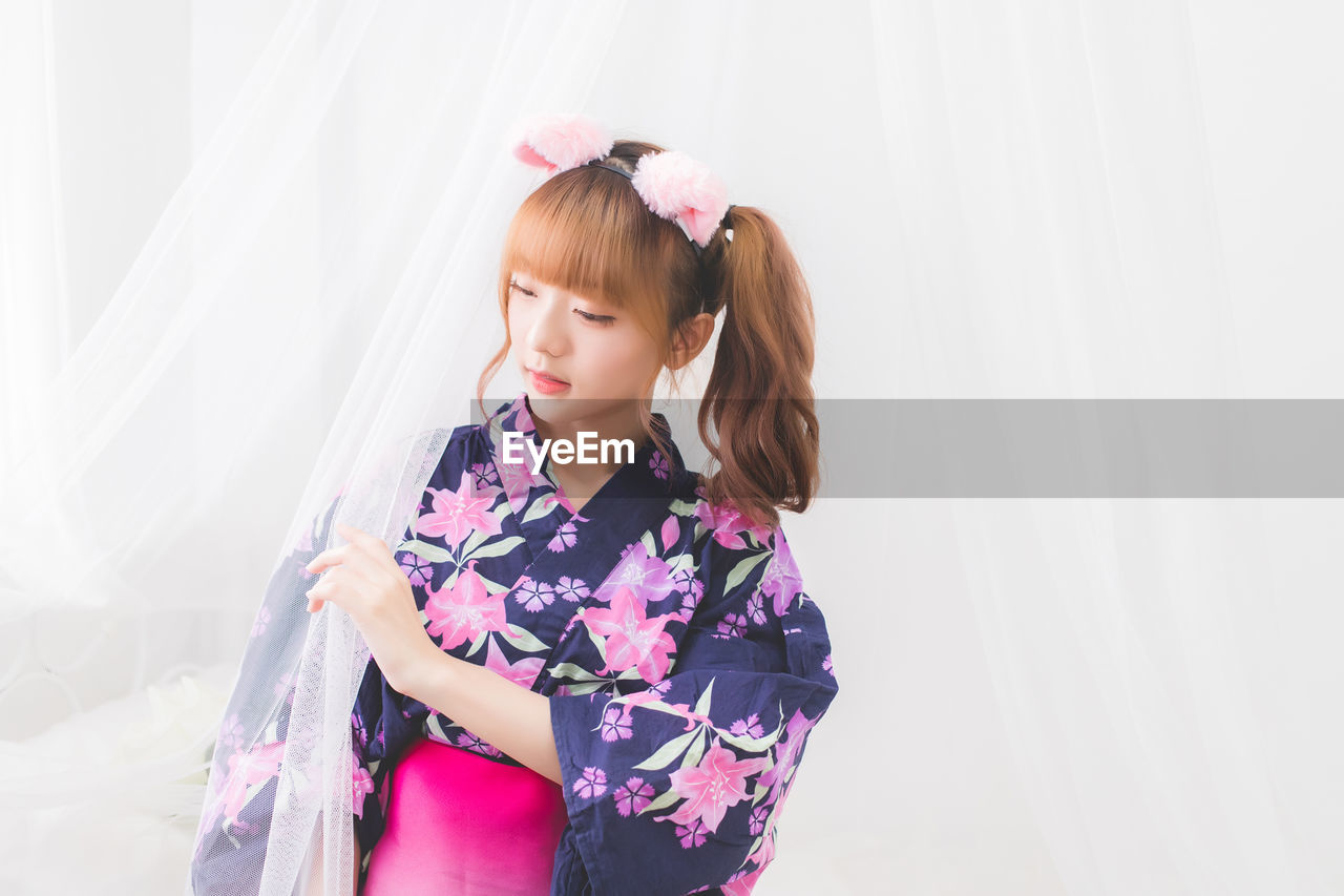 Young woman in costume standing by curtain and window