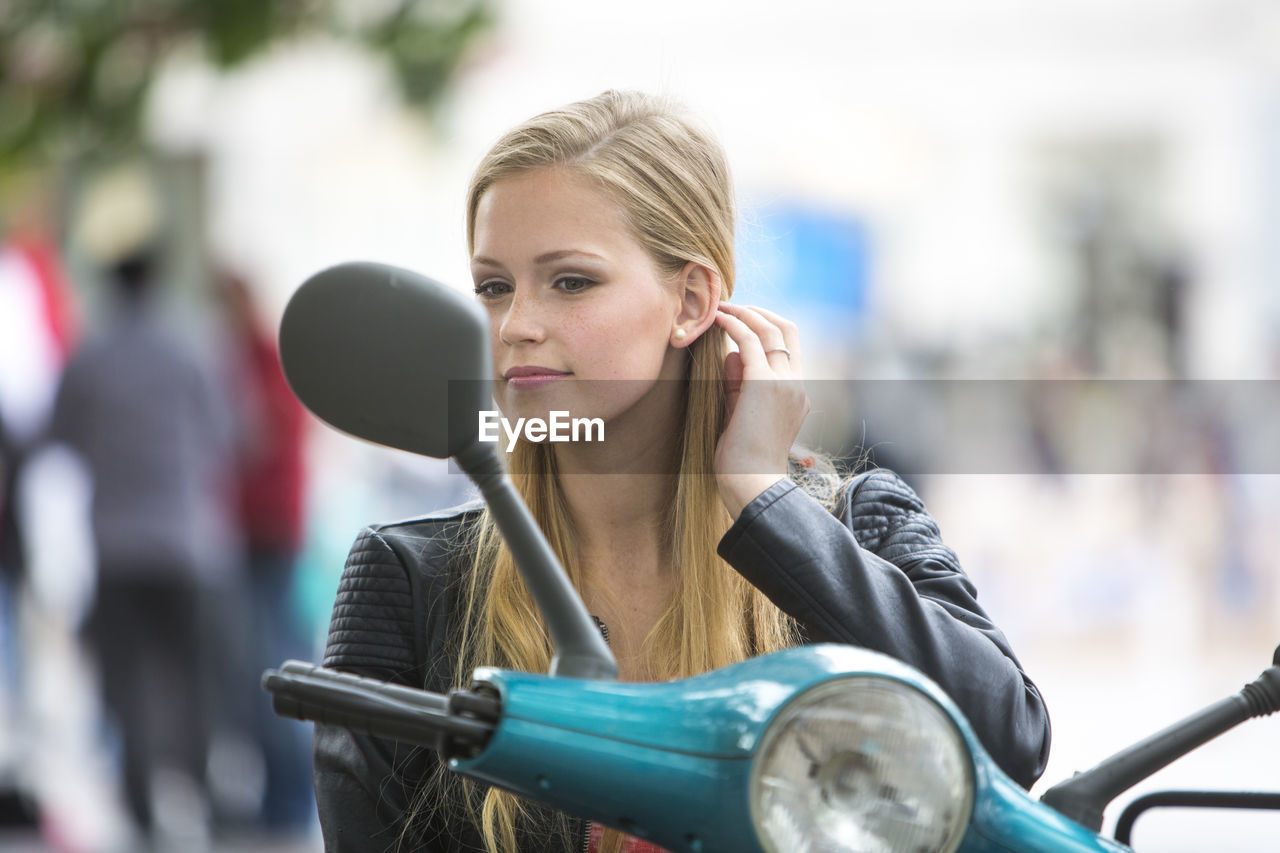 Young woman looking in side-view mirror of motor scooter