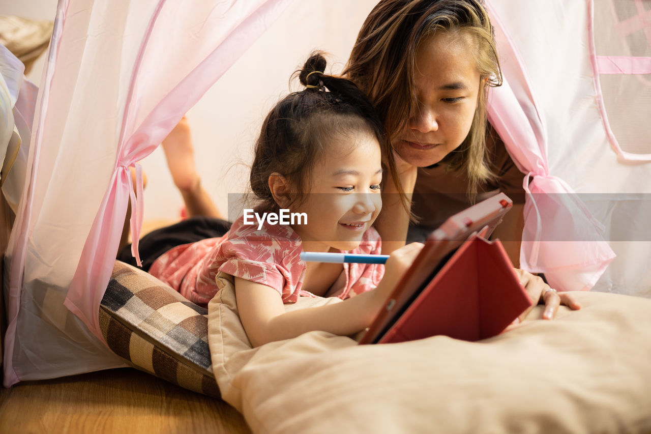 Face focusing on asian mom and adorable daughter are lying on the floor in pink tent at home