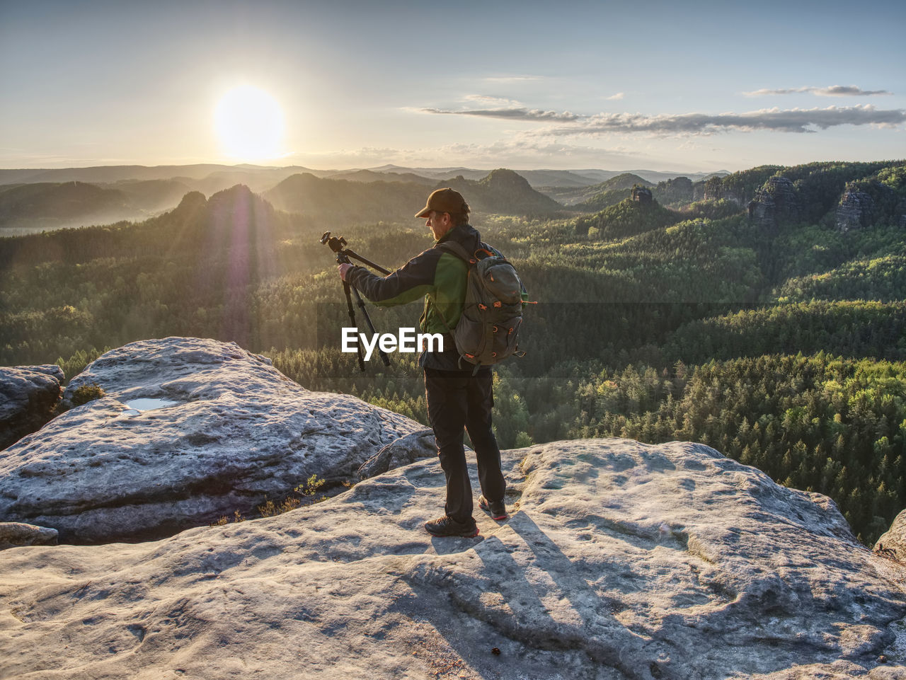 Picture shooting. artist holding camera on tripod and pointing view finder directing into rising sun