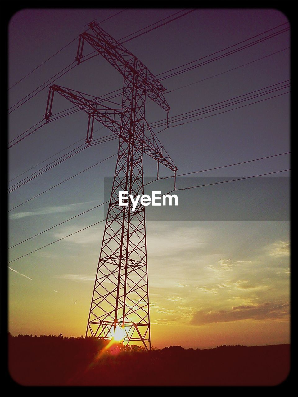 Low angle view of electricity pylon in field against sunset