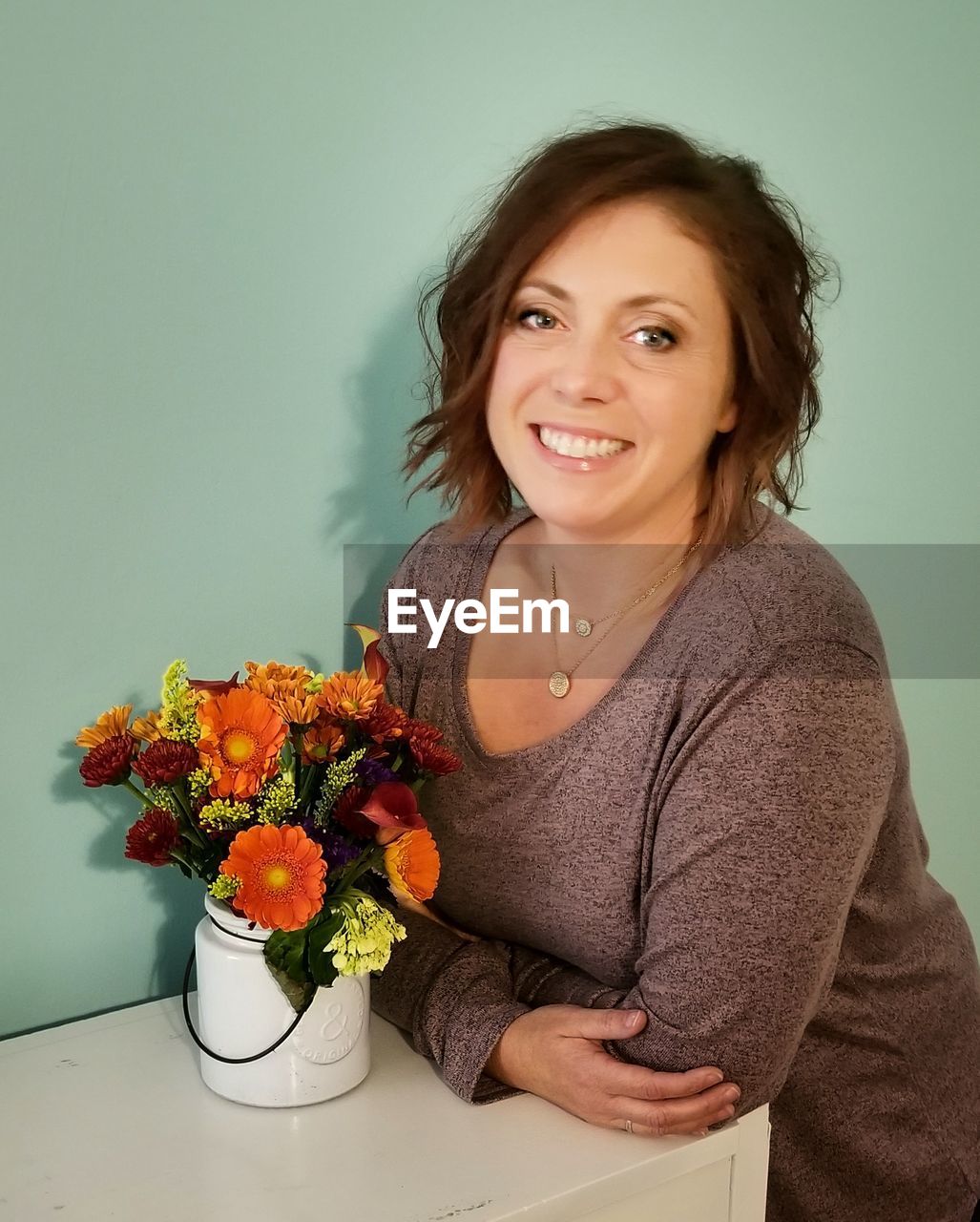 Portrait of smiling woman by flowers in vase on table against wall