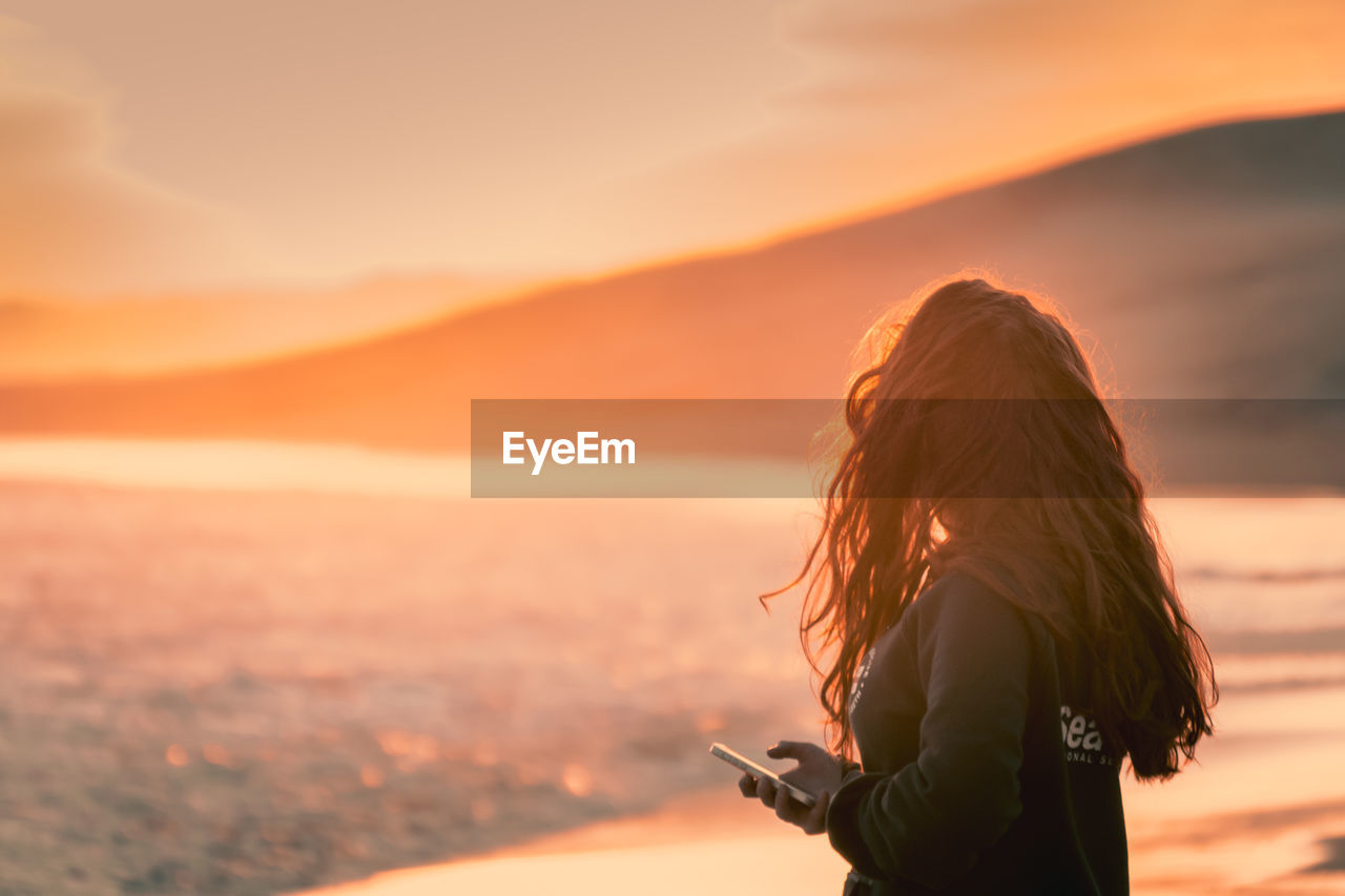 Side view of woman standing on beach during sunset 