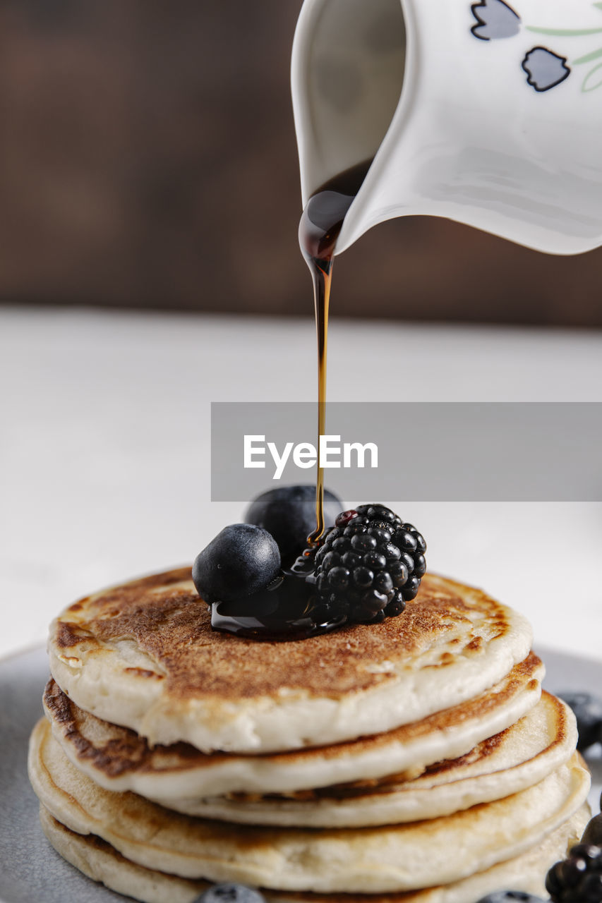 A jar pouring syrup on top of a stack of homemade pancakes with