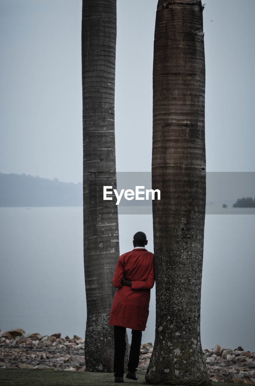 REAR VIEW OF MAN STANDING AGAINST SEA