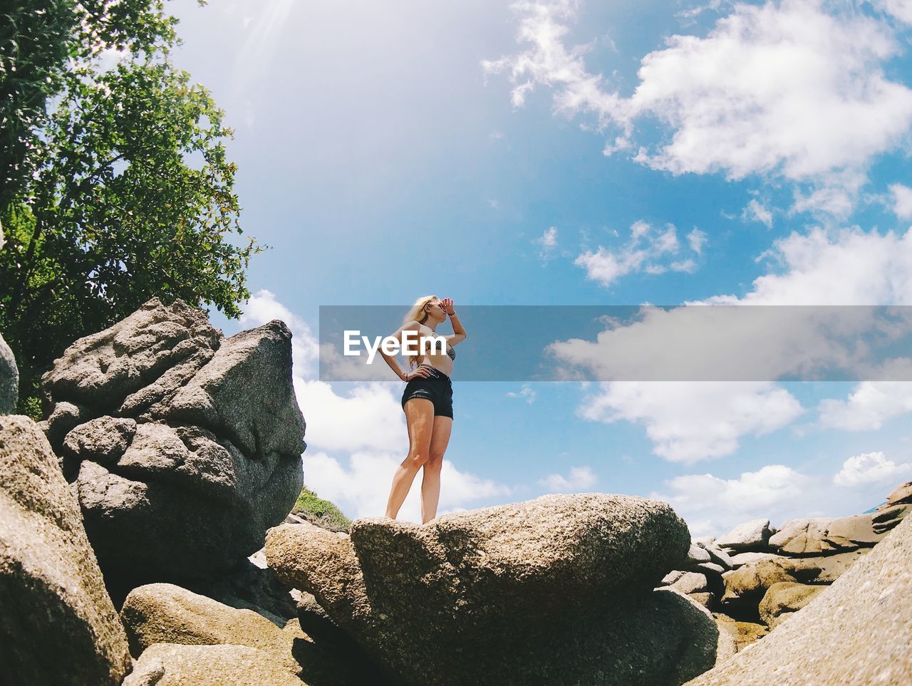 Low angle view of woman standing on rock at beach against blue sky