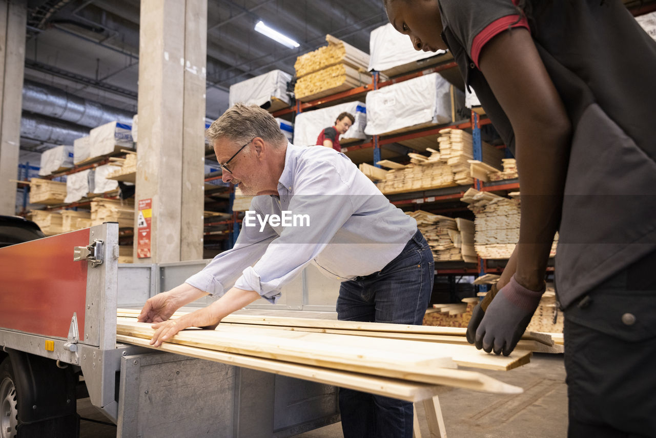 Saleswoman and customer loading wooden plank in trailer at hardware store