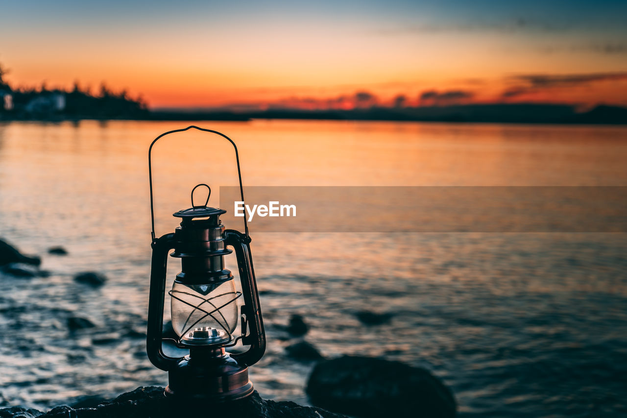 Close-up of lantern by lake against sky during sunset