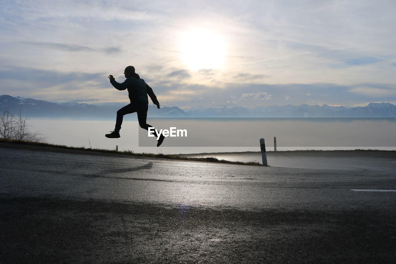 MAN JUMPING ON ROAD AGAINST SKY DURING SUNSET