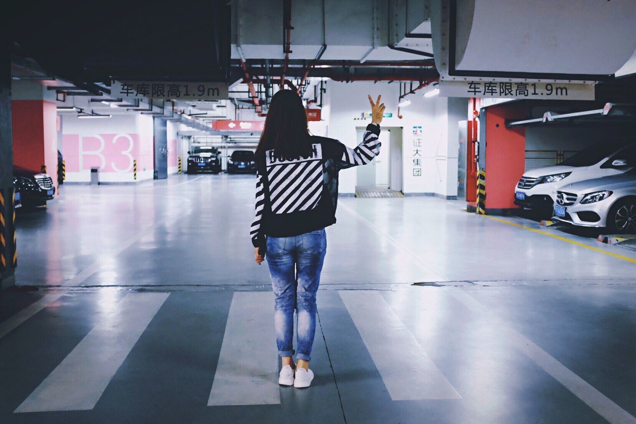 Rear view full length of woman showing peace sign in underground parking lot