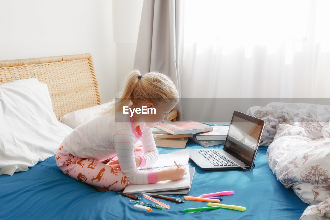 Side view of girl studying with laptop on bed at home
