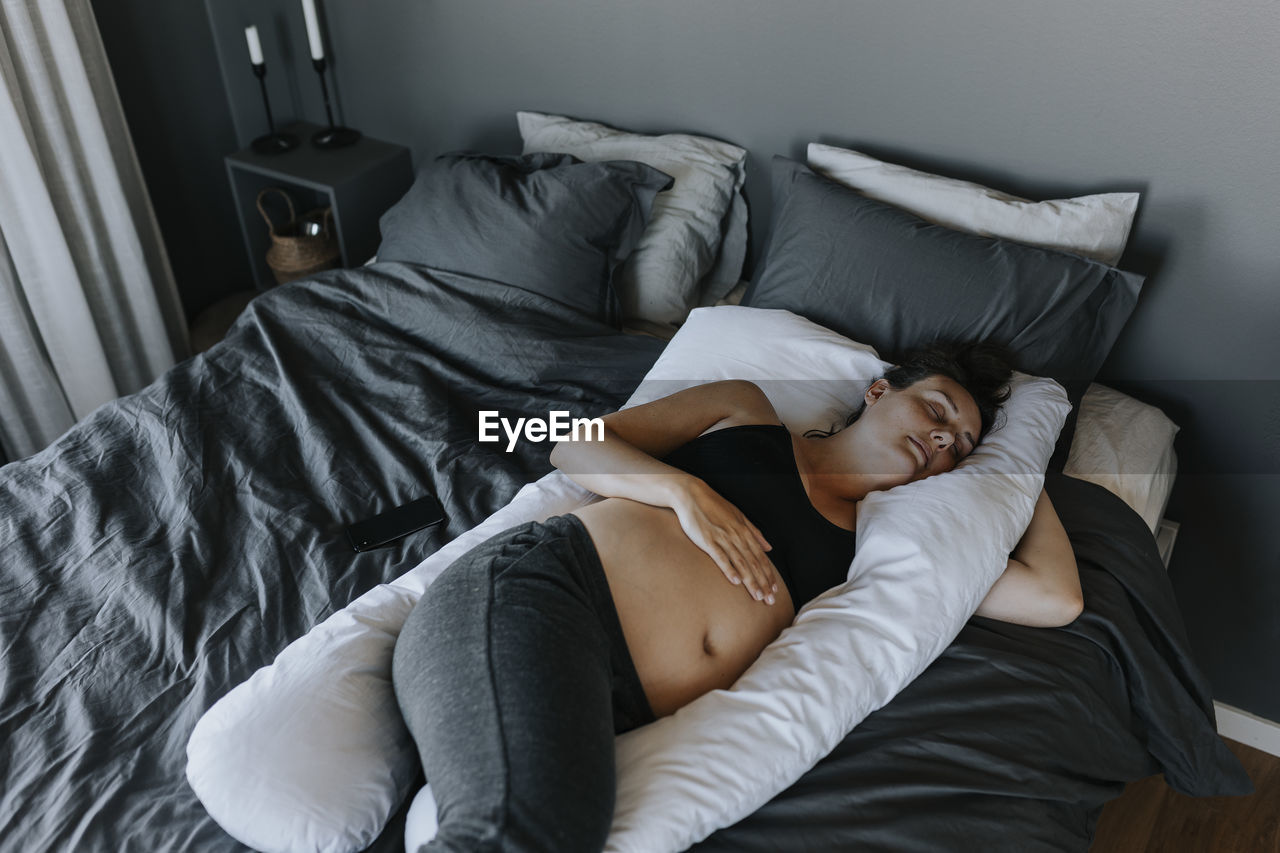 Pregnant woman sleeping on pregnancy pillow on bed