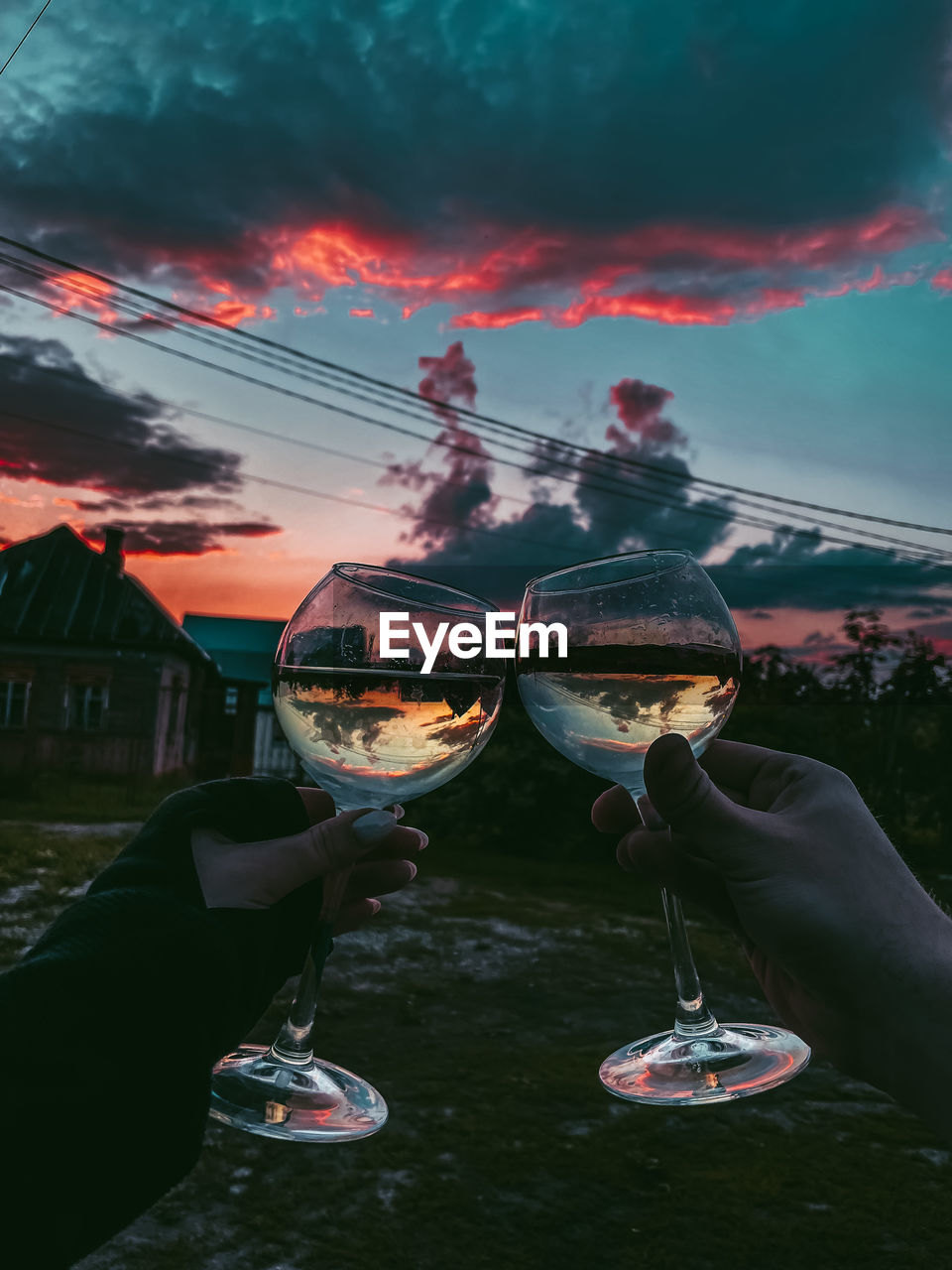 Man holding glass of container against sky at sunset