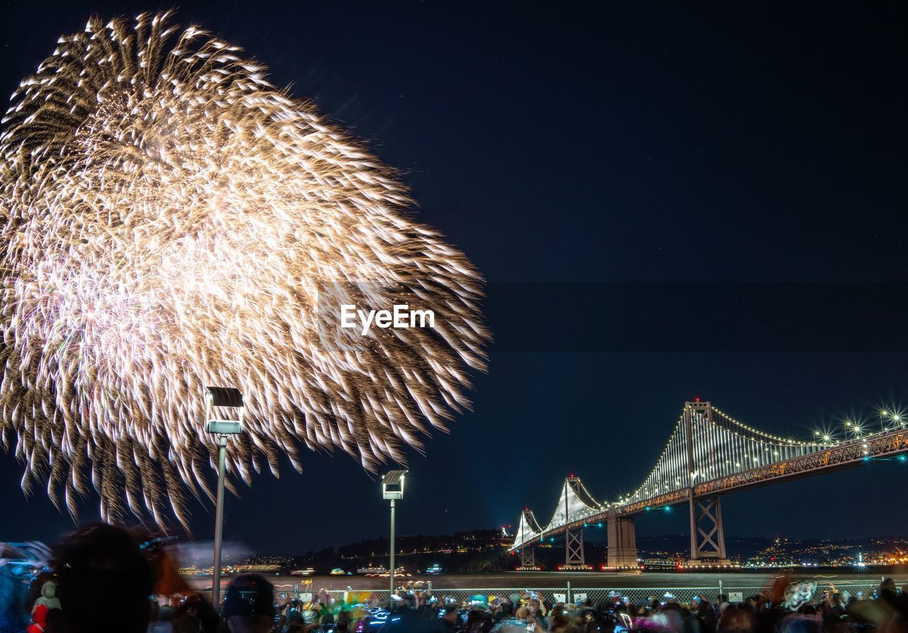 LOW ANGLE VIEW OF FIREWORK DISPLAY OVER BRIDGE AT NIGHT