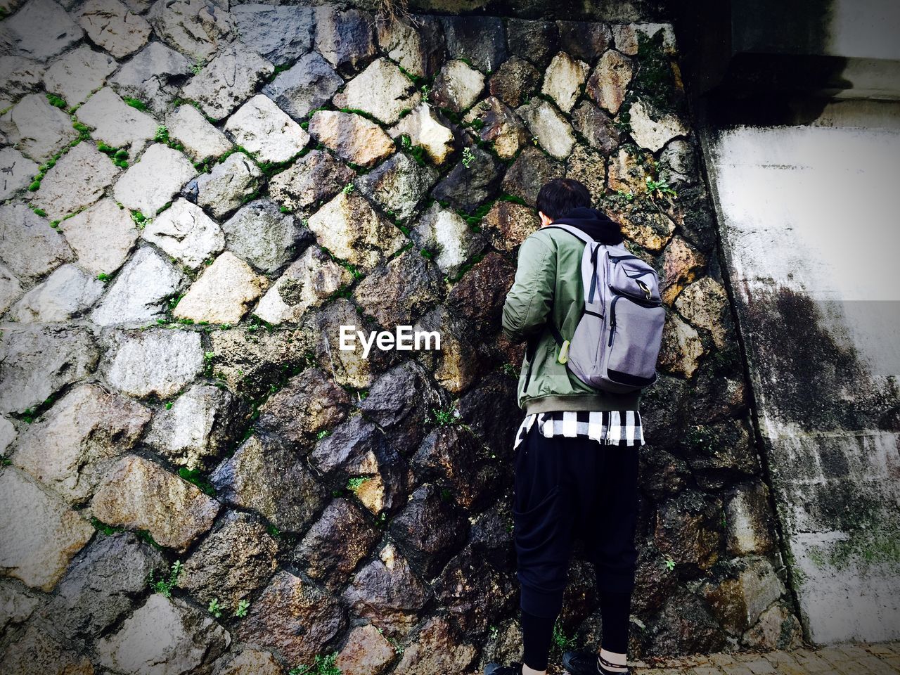 Rear view of man standing against wet stone wall