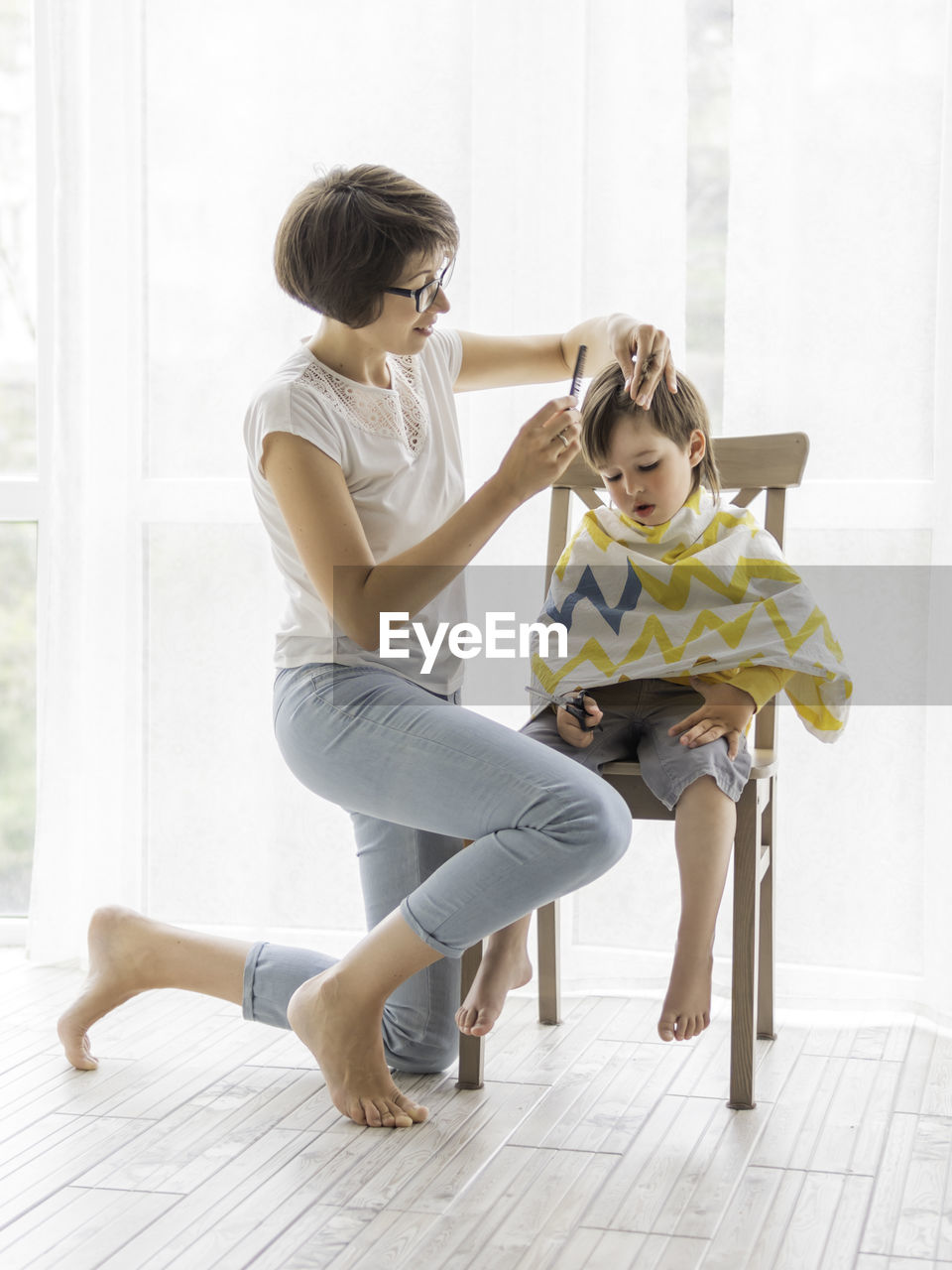 Mother cuts her son's hair by herself. little boy sits and holds pair of scissors. 