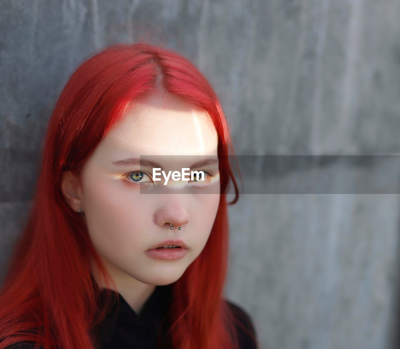 Portrait of a young girl with piercings and red hair, with a ray of sun in her eyes