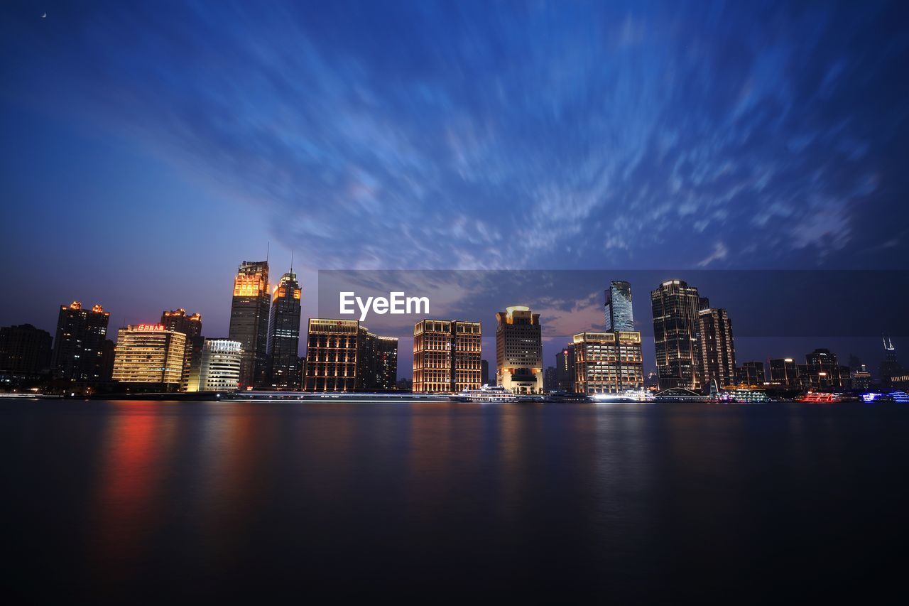 Illuminated buildings by river against sky at night