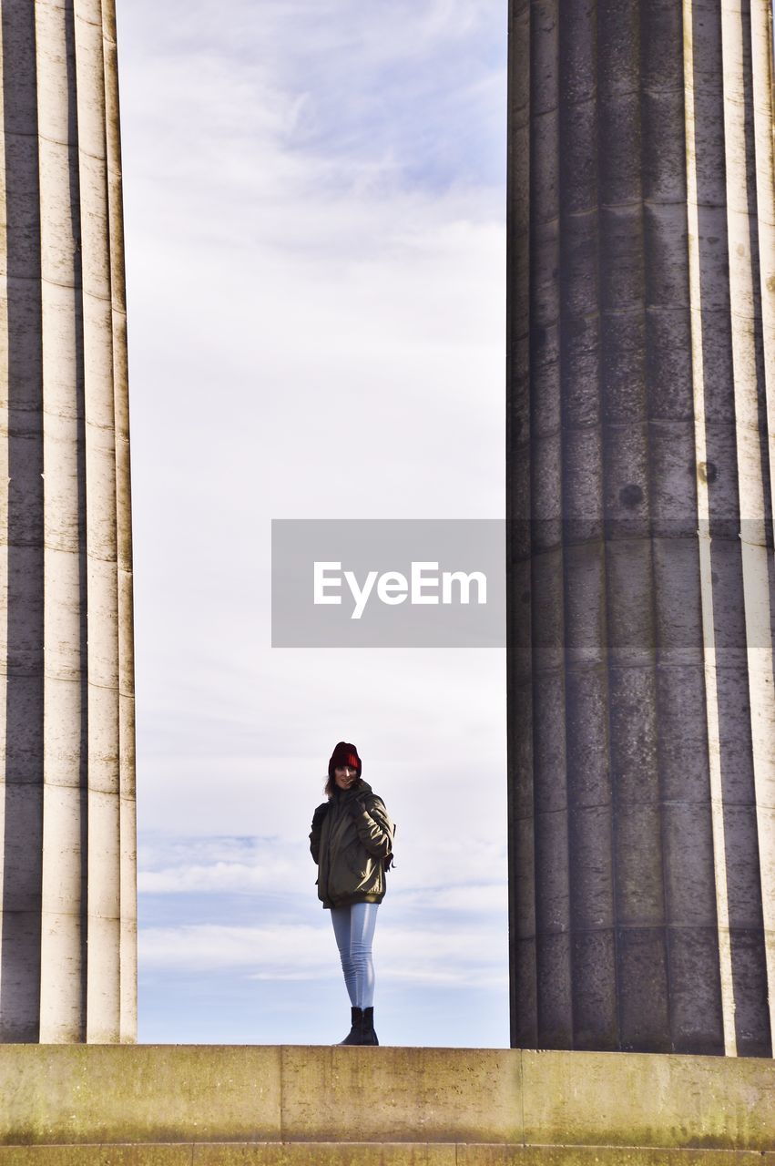 Woman standing amidst columns against sky