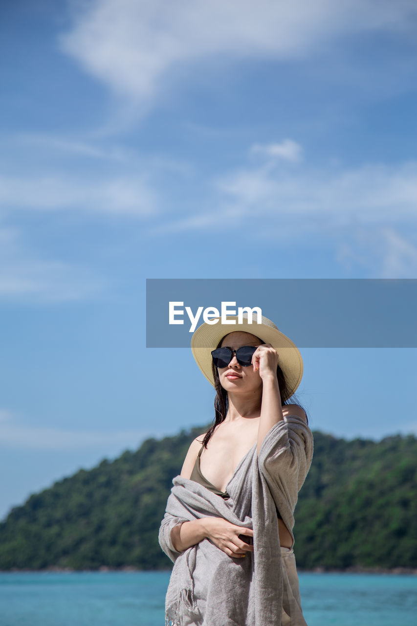 Young woman wearing hat standing against sea