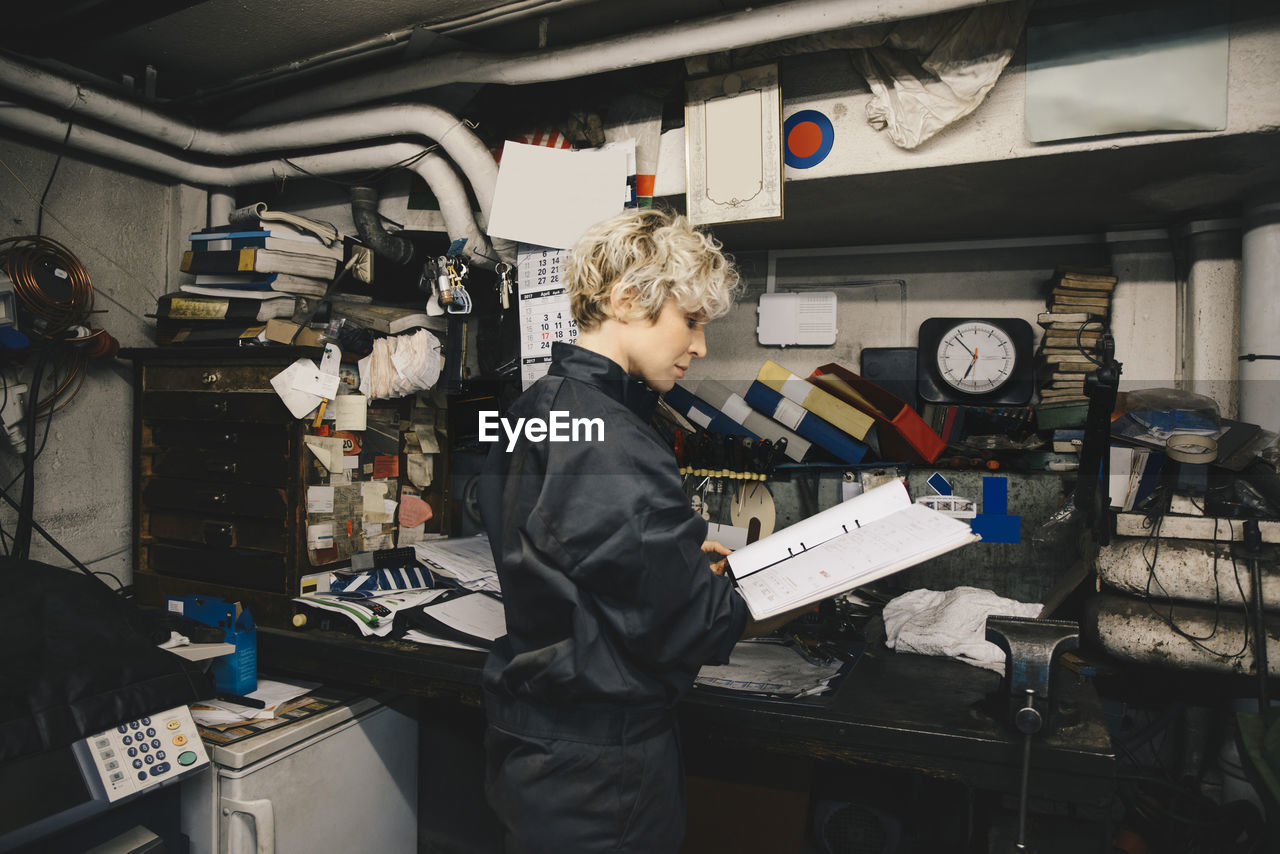 Side view of female mechanic reading document while standing in auto repair shop