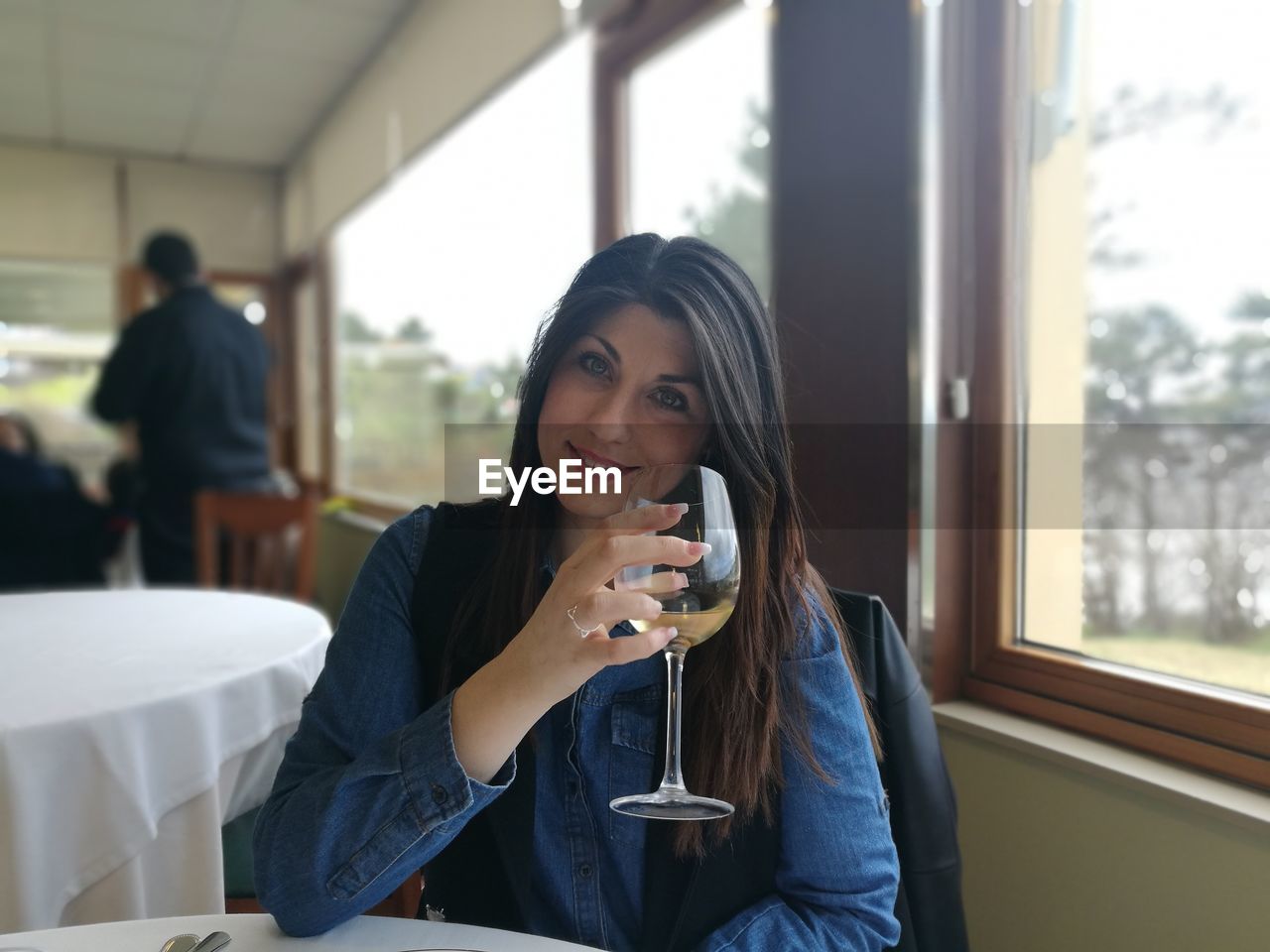 Portrait of young woman holding wineglass while sitting by window in restaurant