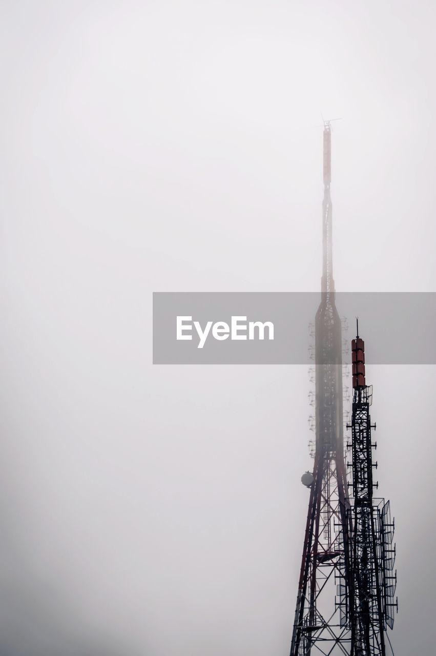 Low angle view of communication towers against sky during foggy weather