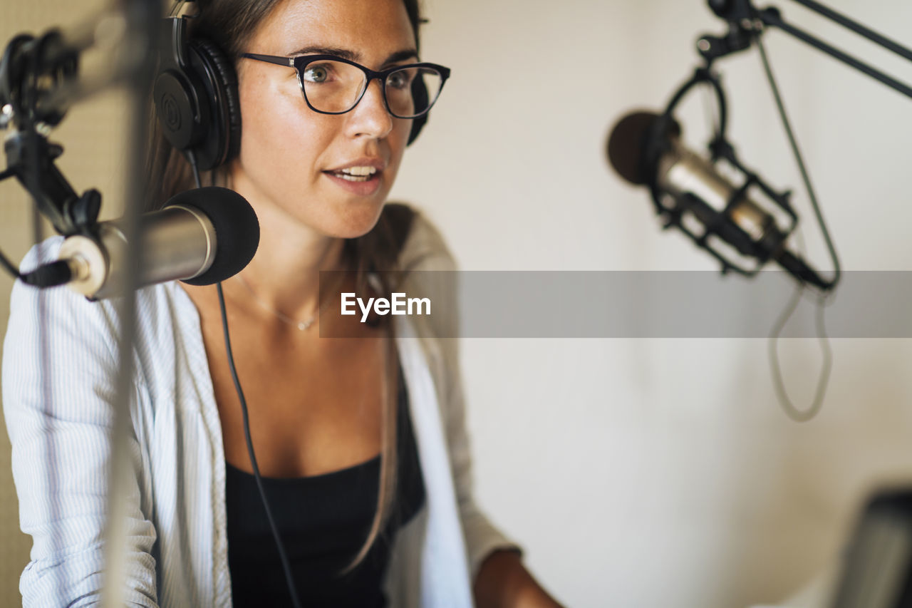 Radio podcast concept - female radio host speaking in microphone in podcasting studio