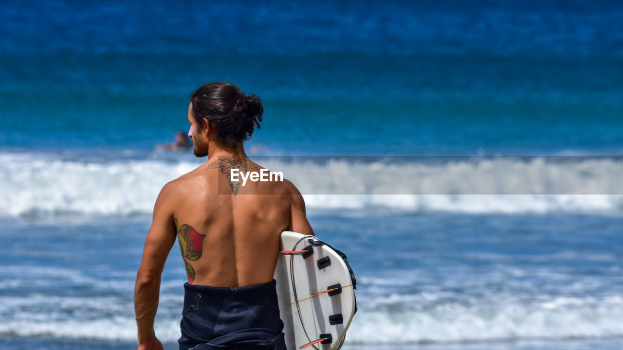 Rear view of man holding surfboard while looking away in sea
