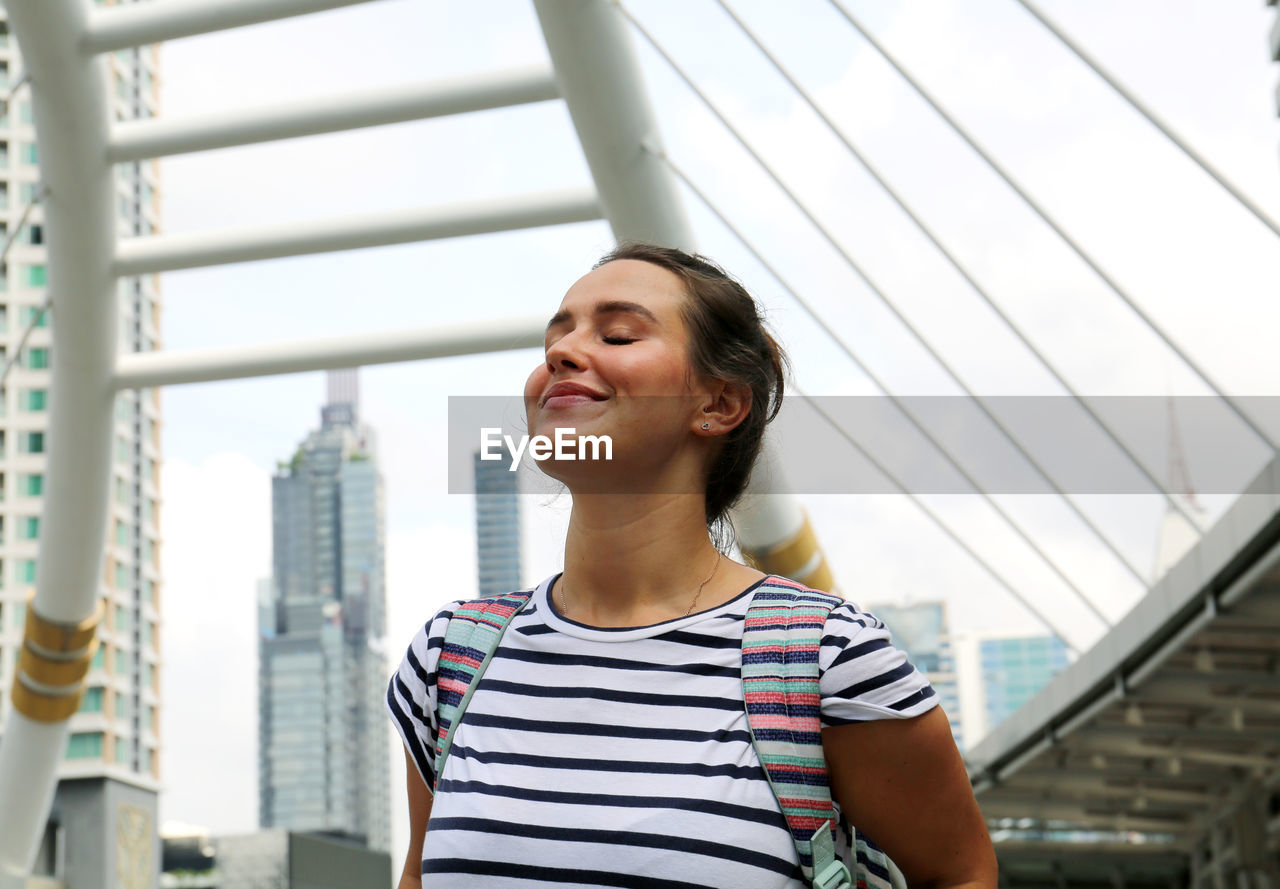 Smiling young with eyes closed woman standing in city