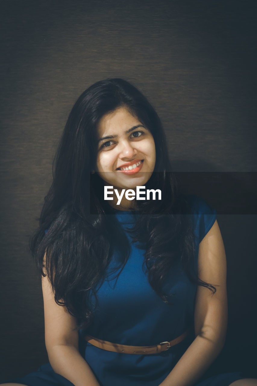 Portrait of smiling young woman against wall