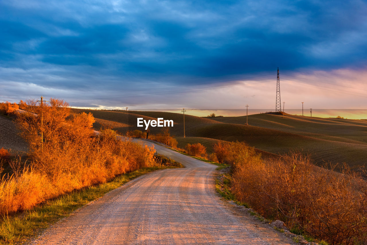 Road amidst field against sky during sunset