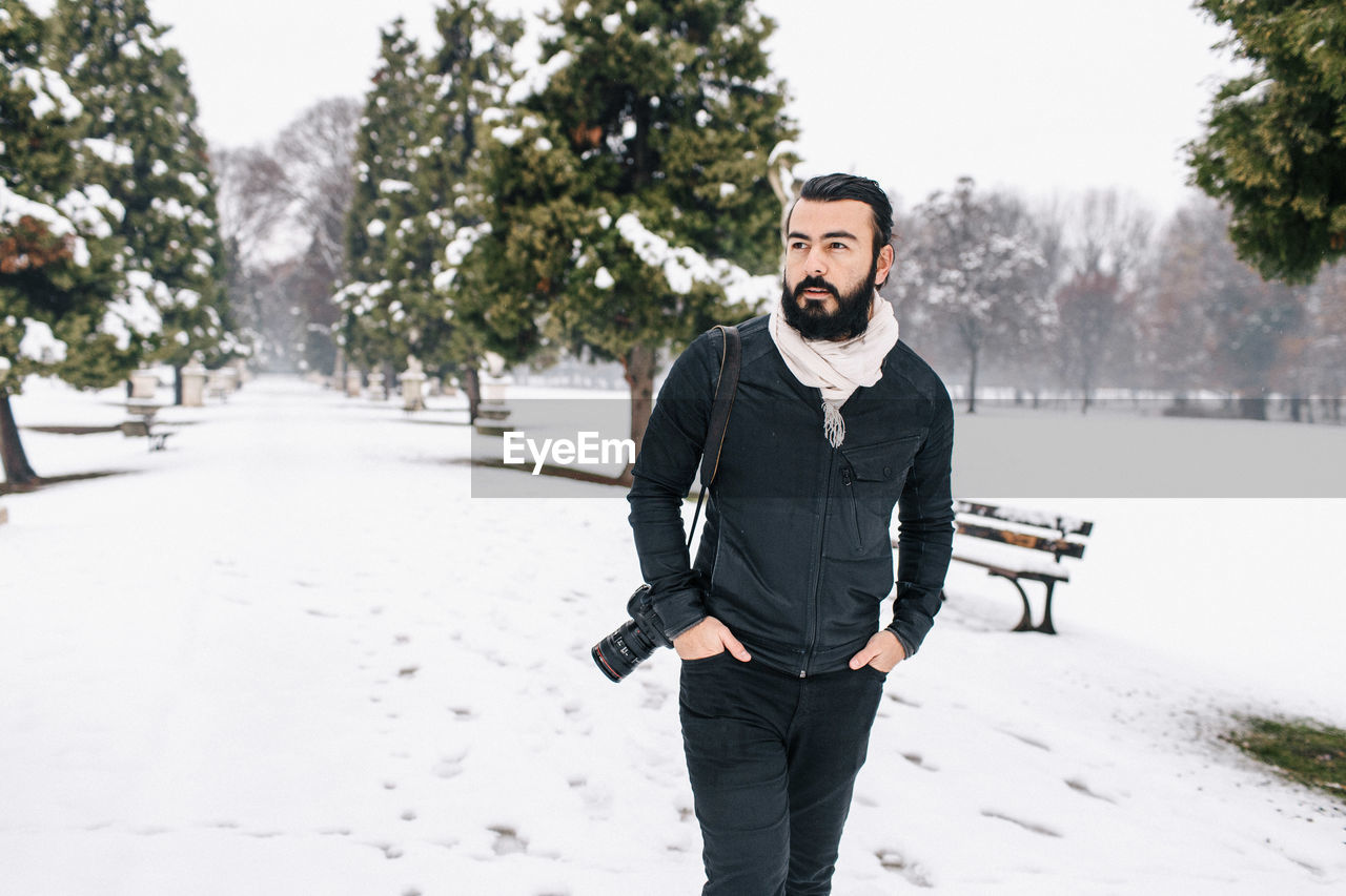 Handsome man with camera standing on snow covered footpath during winter