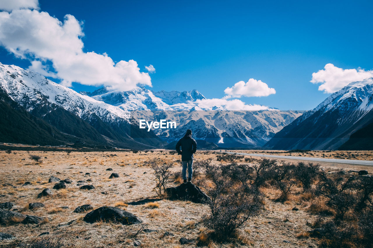 Man standing on field against snowcapped mountains