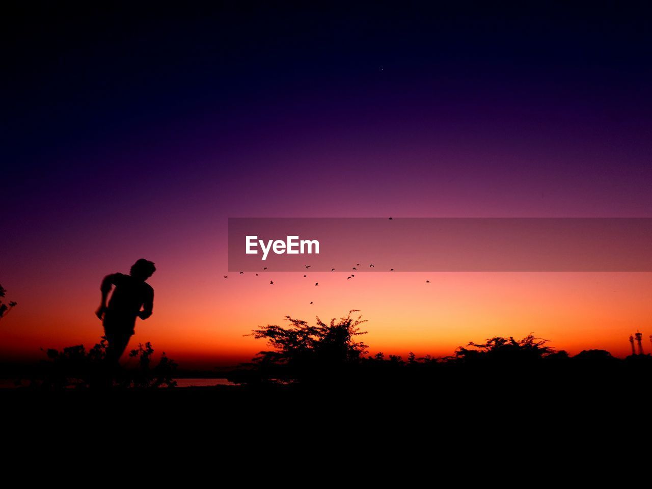 SILHOUETTE MAN STANDING ON FIELD AGAINST ORANGE SKY DURING SUNSET