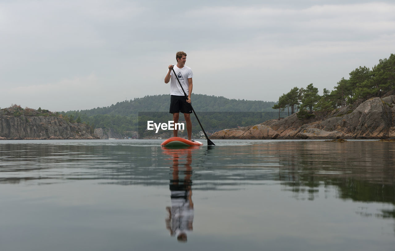 Man paddleboarding in lake against sky