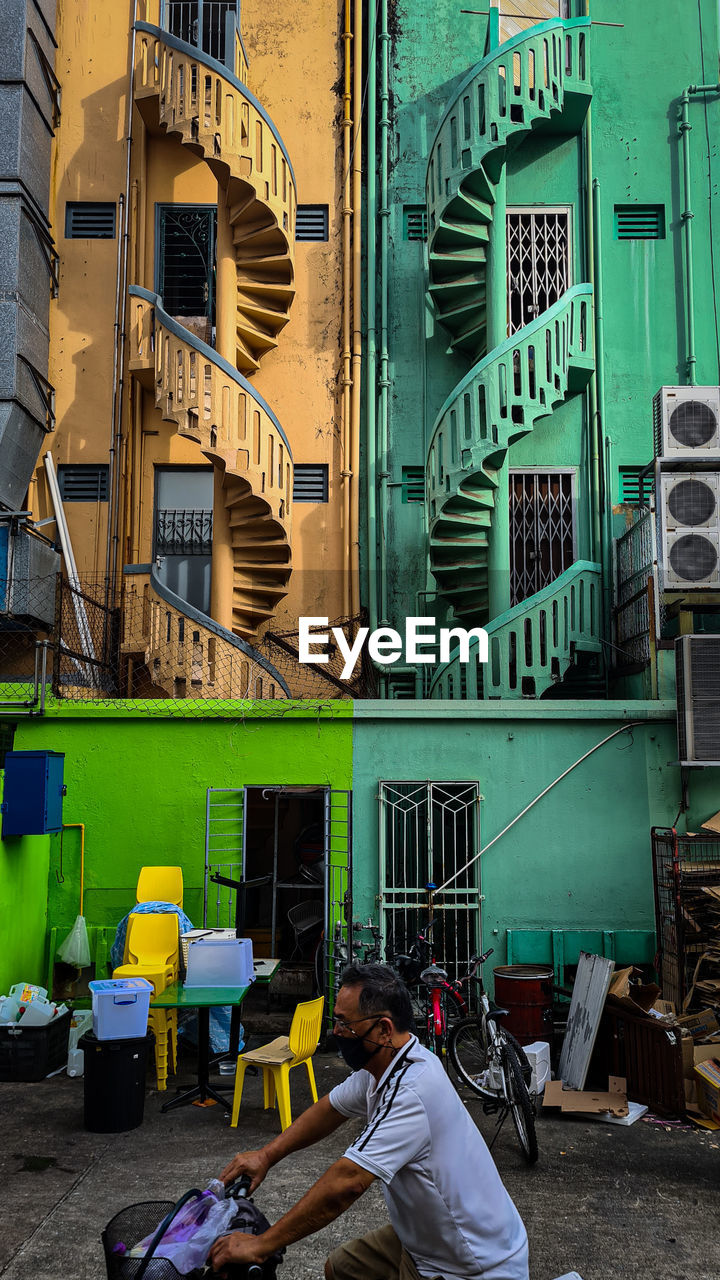 MAN SITTING ON BUILDING BY YELLOW WALL