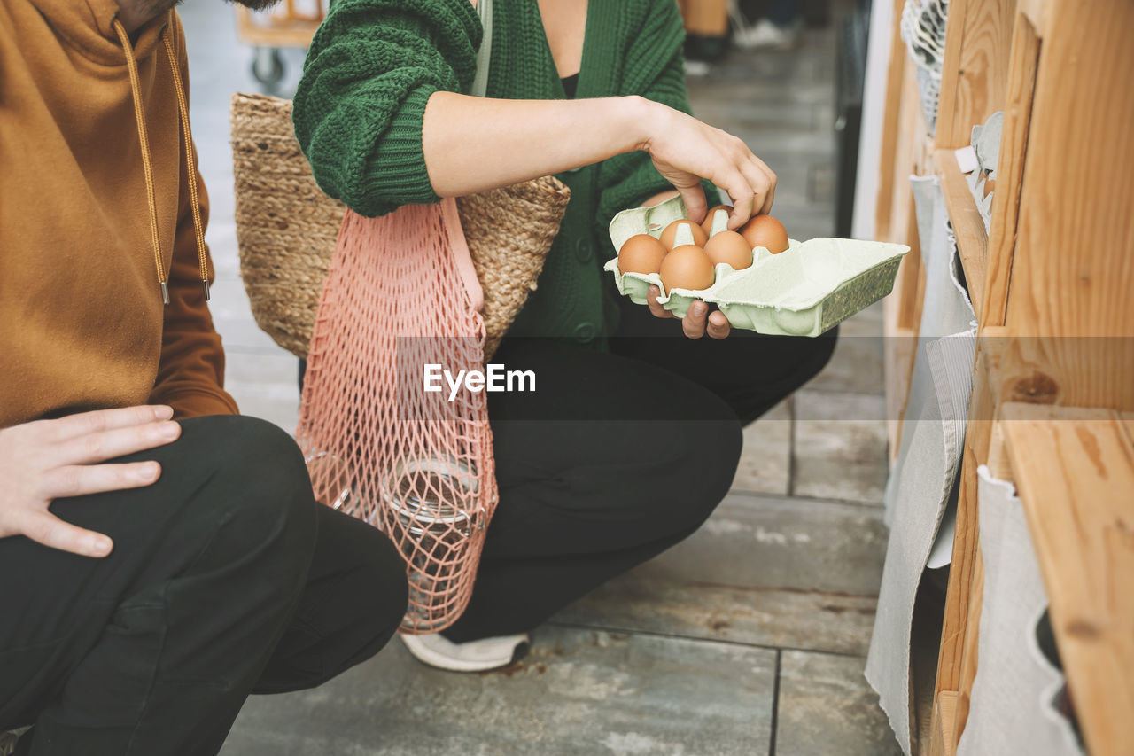 Woman examining eggs in carton by man at shop