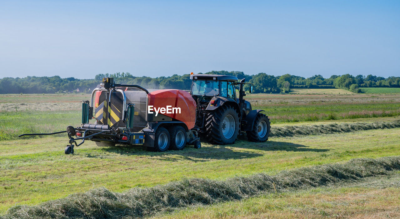 field, agriculture, landscape, rural area, tractor, transportation, farm, rural scene, land, nature, environment, sky, plant, agricultural machinery, transport, agricultural equipment, mode of transportation, machinery, vehicle, land vehicle, crop, day, grass, clear sky, sunny, harvesting, grassland, pasture, blue, plain, no people, prairie, outdoors, scenics - nature, occupation, copy space, sunlight, harvest, travel, growth